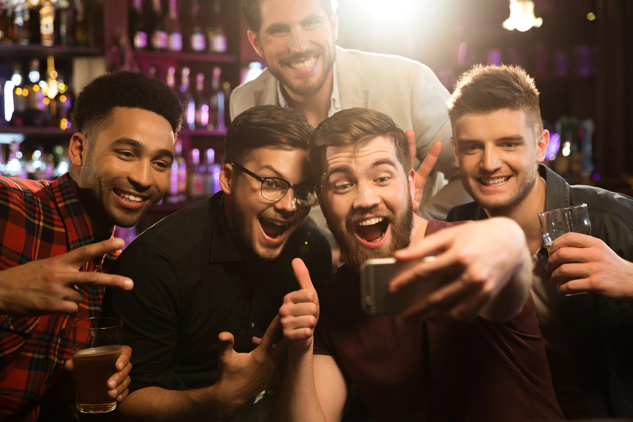 Five friends laughing and taking a selfie together in a bar